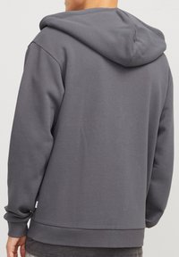 Sweat à capuche gris au toucher doux et avec un cordon de serrage. Poignets et ourlet côtelés, avec une petite étiquette de marque sur le côté. Design simple et minimaliste.