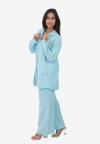 Jasnoniebieski, teksturowany zestaw składający się z koszuli zapinanej na guziki i spodni z szerokimi nogawkami, uzupełniony przez przezroczyste sandały na słupku.