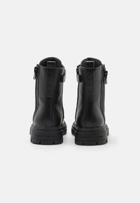 Sorte lær ankle støvler med teksturert overflate, glidelåser på siden og en kraftig gummisåle. Har preget merkevare navn på hælen.