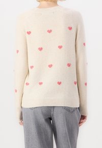 Jasno-beżowy sweter z miękkiego materiału, z rozrzuconymi różowymi motywami serc. Żebrowany dekolt i dół, z luznymi rękawami.