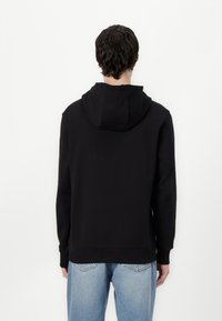 Svart hoodie med känguruficka, ribbad mudd och fåll. Har en stor huva och en avslappnad passform, kombinerad med ljusblå jeans.