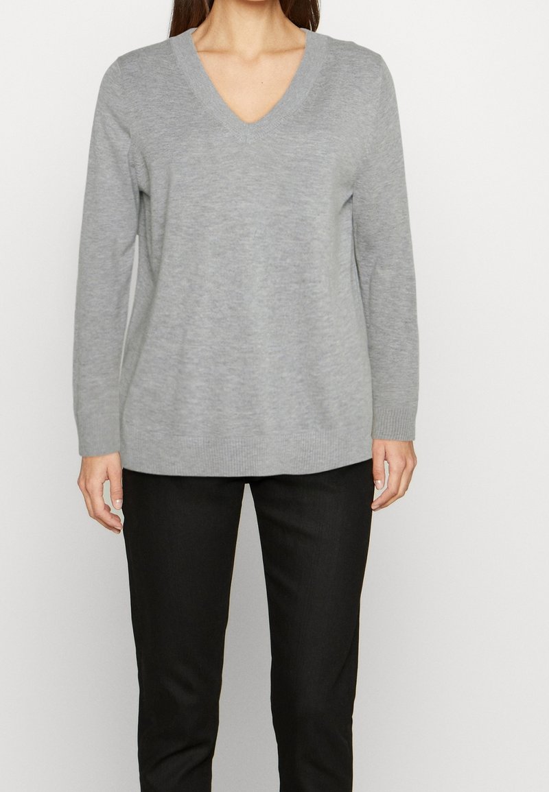 Gray, long-sleeve V-neck sweater made of soft fabric with a relaxed fit, paired with slim black pants, featuring ribbed cuffs and hem.