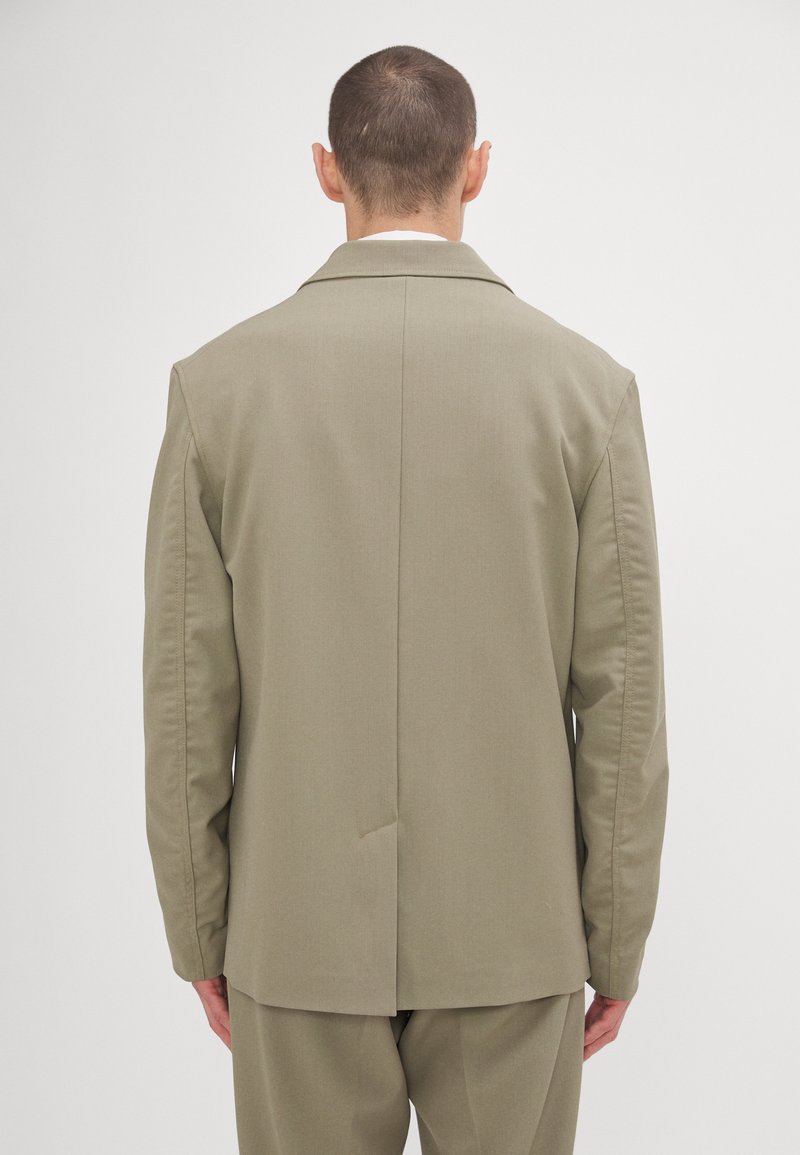 Olivgrüner maßgeschneiderter Blazer mit Reverskragen, Rückenschlitz und strukturierten Schultern. Glattes Material mit einem dezenten Glanz.
