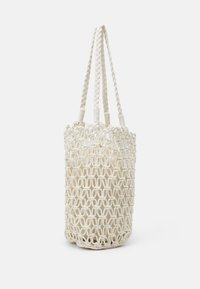 Sac en coton tissé de couleur écrue, en forme cylindrique avec des poignées tressées. Présente un motif de boucles entrelacées, maillage ouvert pour voir l'intérieur.