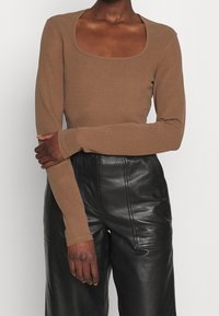 Långärmad brun topp i slät tyg med fyrkantig halsringning, kombinerad med svarta, högmidjade läderbyxor med avslappnad passform.