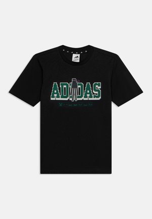 T-shirt noir à manches courtes avec texte vert pixellisé "ADIDAS" et un personnage en pixel art au centre, stylisé comme un graphisme de jeu vidéo.