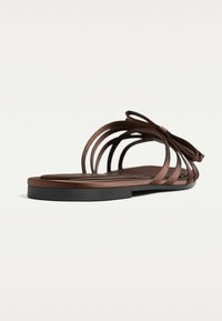Braune flache Sandalen mit einer strukturierten Sohle, geschwungenem Riemendesign und einer Schleifenakzent. Die Riemen sind schlank mit einer glatten Oberfläche.