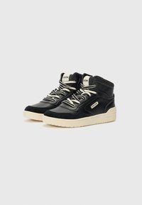 Baskets montantes noires avec une surface texturée, un design perforé, des lacets crème et une semelle beige contrastante avec un détail de marque.