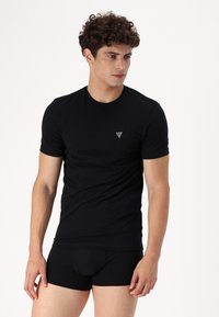 Svart t-skjorte med kort erm og rund hals, med en liten triangel-logo på brystet, sammen med svarte tettsittende shorts.