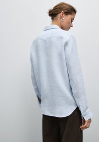 Camicia azzurra chiara a maniche lunghe realizzata in un tessuto texture con colletto e orlo arrotondato. Presenta polsini con bottoni e una vestibilità comoda.