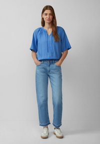 Blusa blu chiaro a maniche corte con scollo a V e cordoncino, abbinata a jeans blu chiaro a vita alta a gamba dritta e sneakers bianche.