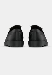 Zwarte leren schoenen met een lage hak, ronde neus en een gladde textuur. Voorzien van een gestikte naad en een licht verhoogde achterkant.