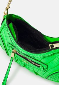 Borsa in pelle verde con stampa coccodrillo e finitura lucida. Caratterizzata da una cerniera dorata e una tracolla a catena, con un interno trapuntato nero.