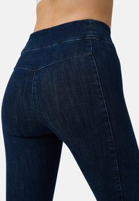 Jeans in denim blu scuro con vita alta, caratterizzati da cuciture a contrasto e una texture liscia. La forma enfatizza un design aderente.