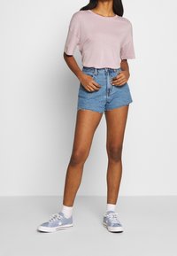 Roze T-shirt met korte mouwen, hoge denimshorts met een rafelige zoom, en lichtblauwe sneakers met witte accenten en veters.