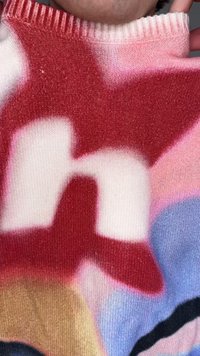 Värvikas kootud kampsun, millel on suured abstraktsed vormid punases, valges, roosas, sinises, pruunis ja mustas, hoituna inimese kaela lähedal.