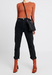 Vaqueros negros de cintura alta con dobladillos enrollados, combinados con una blusa naranja de manga larga de canalé. Los accesorios incluyen un pequeño bolso negro y botas rojas brillantes.