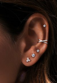 Boucles d'oreilles en argent présentées sur une oreille, ornées de plusieurs clous en cristal de différentes tailles et d'un bracelet à design torsadé.