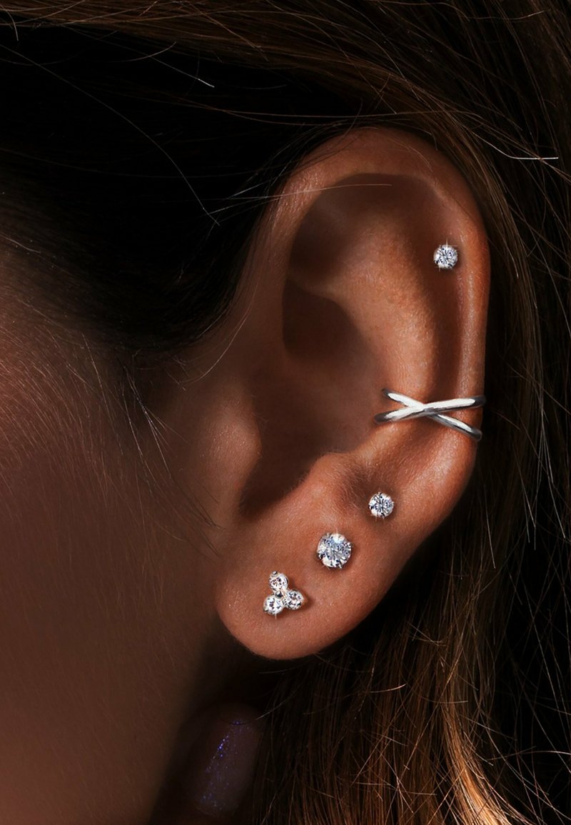 Boucles d'oreilles en argent présentées sur une oreille, ornées de plusieurs clous en cristal de différentes tailles et d'un bracelet à design torsadé.
