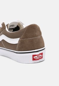 Baskets en daim marron avec des accents blancs, dotées d'un col rembourré, d'une bordure noire et d'une étiquette logo Vans rouge sur le talon.