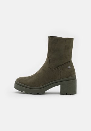Bottine en daim vert olive avec talon bloc épais, fermeture éclair latérale et semelle crantée.