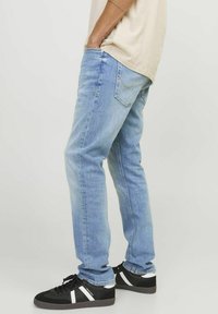 Vaqueros de denim azul claro con corte recto, diseño de cinco bolsillos y costuras visibles. Combinados con zapatillas negras y blancas.