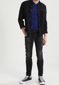 Mustapaita sinisen poolopaidan päällä, yhdistetty tummiin skinny-farkkuihin ja mustiin lenkkareihin, joissa on valkoisia yksityiskohtia. Silkkinen kangas ja kiinteä muotoilu.