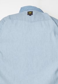 Hellblaues Jeanshemd auf der Rückseite mit einem umgeklappten Kragen und einem schwarzen Lee-Markenlabel in der Nähe des Halsausschnitts.