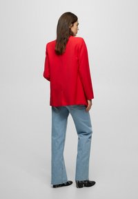 Rød skræddersyet blazer med lange ærmer, bagslidser og glat tekstur, parret med lyseblå højtaljede jeans og sorte ankelstøvler.