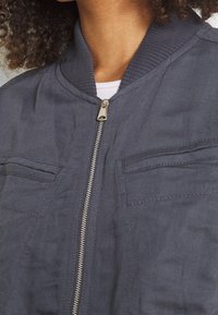 Chaqueta de piloto navy con cuello acanalado, cierre de cremallera frontal, dos bolsillos en el pecho y tejido texturizado. Presenta un diseño minimalista.