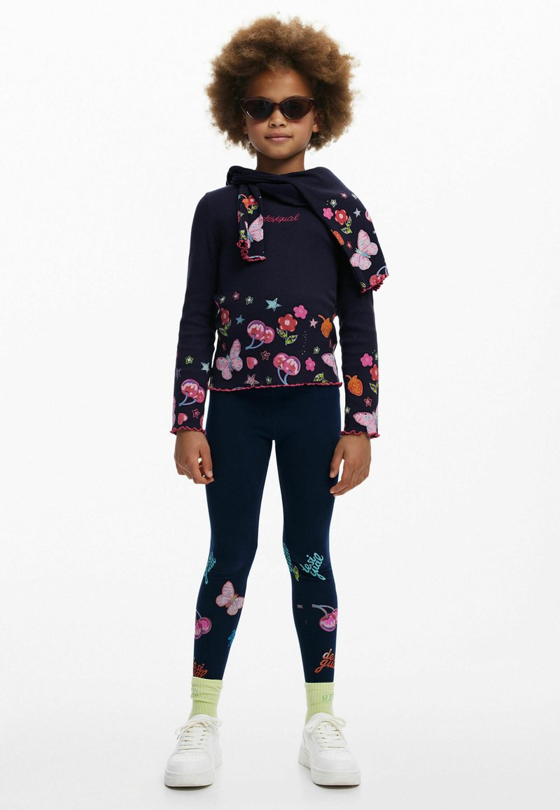 Marinefarbener Langarmoberteil mit Blumen- und Schmetterlingsmotiven, kombiniert mit marineblauen Leggings mit bunten Mustern und engen Bündchen. Weiße Sneakers.