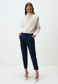 Un haut sans manches en tricot crème porté sur une chemise blanche associé à un pantalon bleu marine. Des escarpins crème à bout pointu complètent le look.