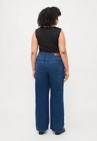 Black sleeveless top paired with wide-leg blue denim jeans. The jeans feature a brown leather patch on the back and two rear pockets.