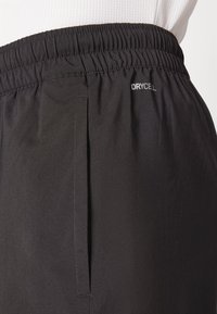 Crne sportske kratke hlače s elastičnim pojasom, bočnim džepovima i logom "DRYCELL". Glatka, lagana tkanina s mat završetkom.