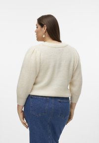Maglione color crema, con texture, maniche a sbuffo, scollatura rotonda e polsini a coste, abbinato a jeans in denim blu con tasche posteriori.
