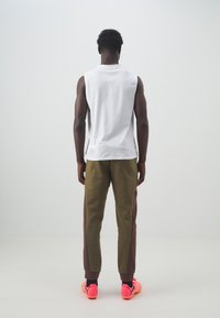Débardeur de sport blanc sans manches associé à un pantalon de jogging vert olive avec des panneaux latéraux bordeaux, des accents noirs et des chaussures de couleur rose vif.