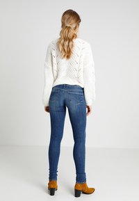 Blå denim skinny jeans parat med en vit kabelstickad tröja. Jeansen har en klassisk femficksdesign och subtila sömnadsdetaljer.