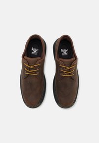 Rjave usnjene čevlje z okroglimi konicami, rumenimi vezalkami in črnimi gumijastimi podplati. Imajo gladko teksturo in šivane podrobnosti.