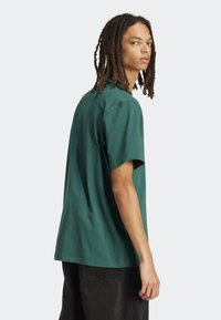 Maglietta di cotone verde a maniche corte, vestibilità comoda e scollo rotondo. La vista posteriore mostra cuciture minime e una texture liscia.