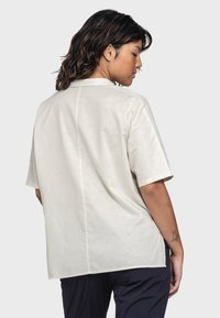 Cream-colored short-sleeve shirt with a relaxed fit, featuring a hidden seam down the back and soft, smooth texture.