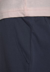 Baumwollmischgewebe-Kleidung mit einem hellrosa Oberteil und dunklen Marinehosen. Das Oberteil hat einen dezenten Saumstich; die Hosen verfügen über Seitentaschen.