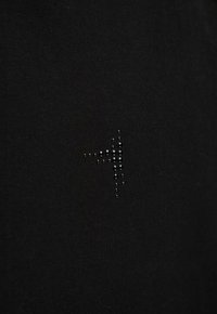 Czarny materiał z małym, błyszczącym wzorem wypukłych kropek, tworzącym strzałkę skierowaną w prawo, blisko środka.