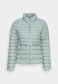 Veste matelassée bleu clair avec un col haut, un motif matelassé horizontal et deux poches zippées. Fermeture par une fermeture éclair frontale avec une quincaillerie argentée.
