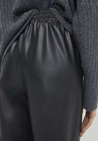 Svarta läderbyxor med en samlad midja, kombinerat med en mjuk grå stickad tröja, som visar textur och eleganta design detaljer.