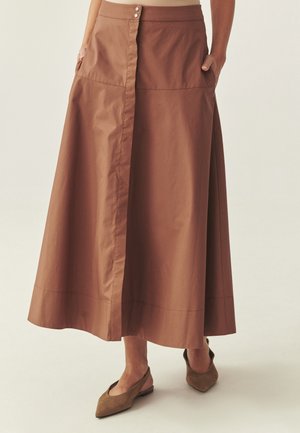 Jupe maxi en coton marron avec fermeture à boutons, poches latérales et coupe droite. Texture lisse et coutures visibles le long de l'ourlet.