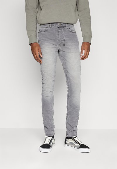 Jeans in denim grigio con finitura sbiadita, design slim fit, cinque tasche e chiusura a bottone classica, abbinati a sneakers in bianco e nero.
