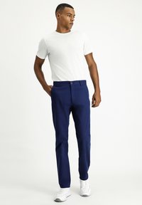 Chino blu navy in misto cotone con vestibilità dritta, dotati di una classica chiusura a bottone e tasche laterali, abbinati a una t-shirt bianca.