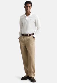 Pitkähihainen valkoinen poolopaita kauluksella, yhdistetty ruskeisiin chinoihin ja ruskeaan vyöhön. Asuun kuuluu mustat kengät, joissa on keltaisia yksityiskohtia.