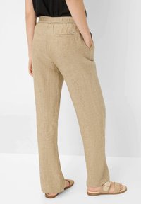 Jasnobeżowe lniane spodnie o luźnym kroju, z elastycznym pasem, bocznymi kieszeniami oraz tylną kieszenią. Noszone z jasnobrązowymi sandałami.