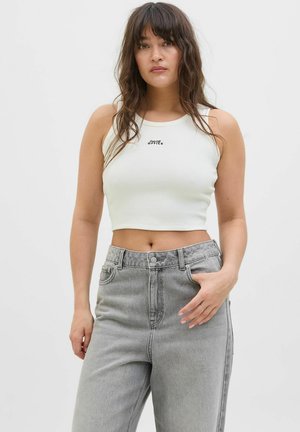 Vitt ribbat crop-top med rund halsringning och svart tryckt text, kombinerat med ljusgrå högmidjade jeans. Strukturen ser slät ut.